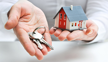 A person holds a house key in one hand and a small model house in the other